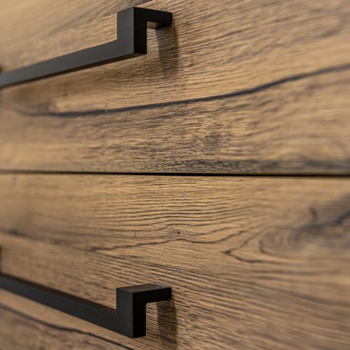 Wooden chest of with drawers with black handles close up.